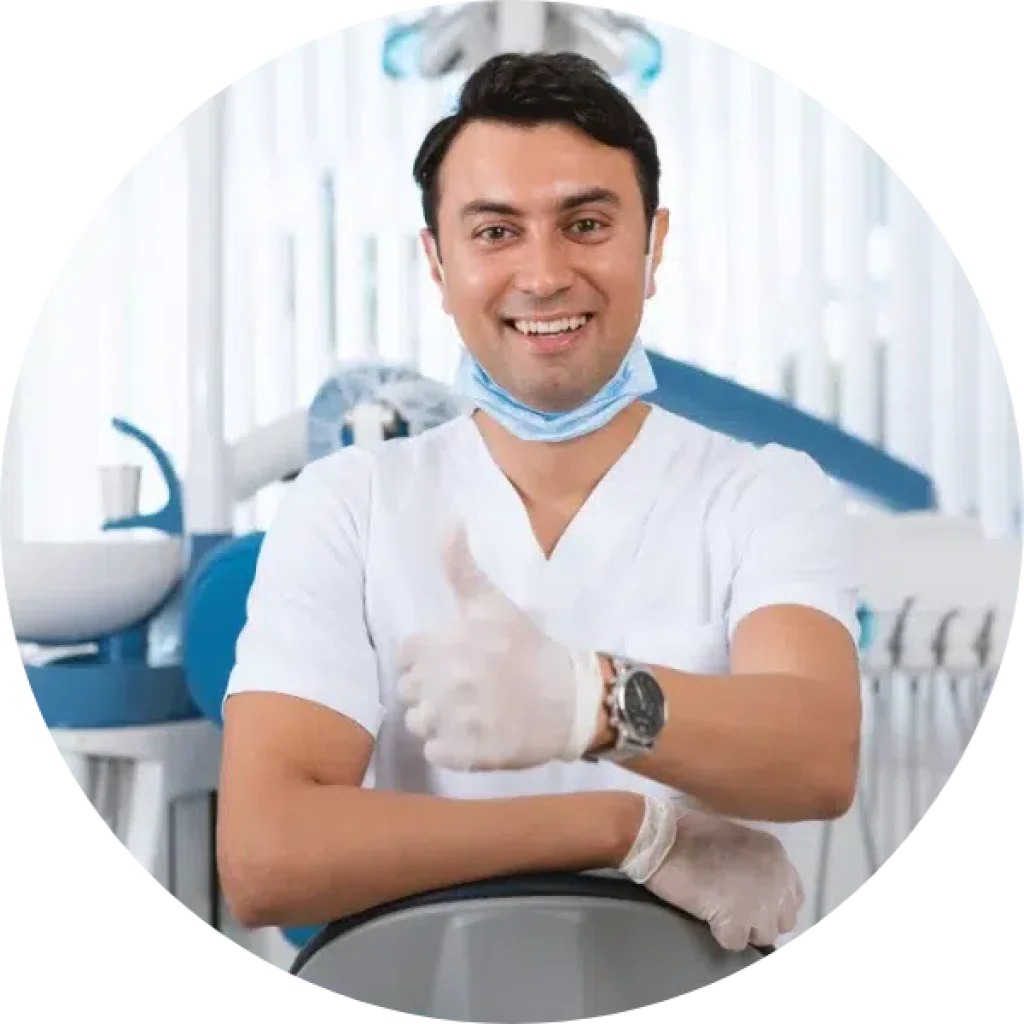 Dentista con bata y guantes blancos, mascarilla en el cuello, sonr&iacute;e y levanta el pulgar en la consulta con herramientas NSK. | La muela